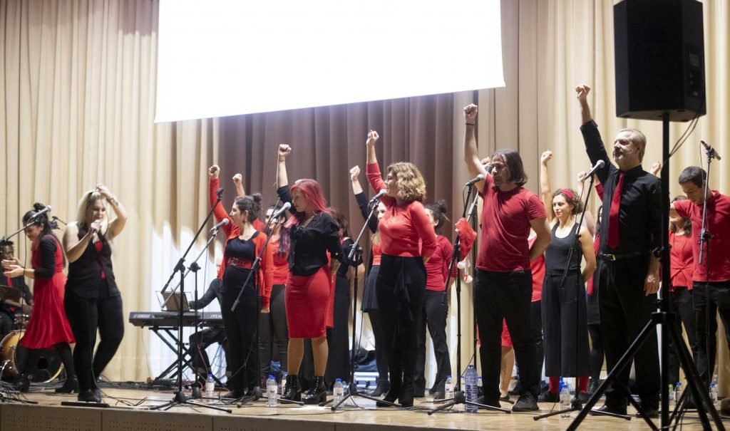 Integrantes Fundación porqueViven en el escenario, brazo en alto, con micrófonos y equipo ante una pantalla blanca