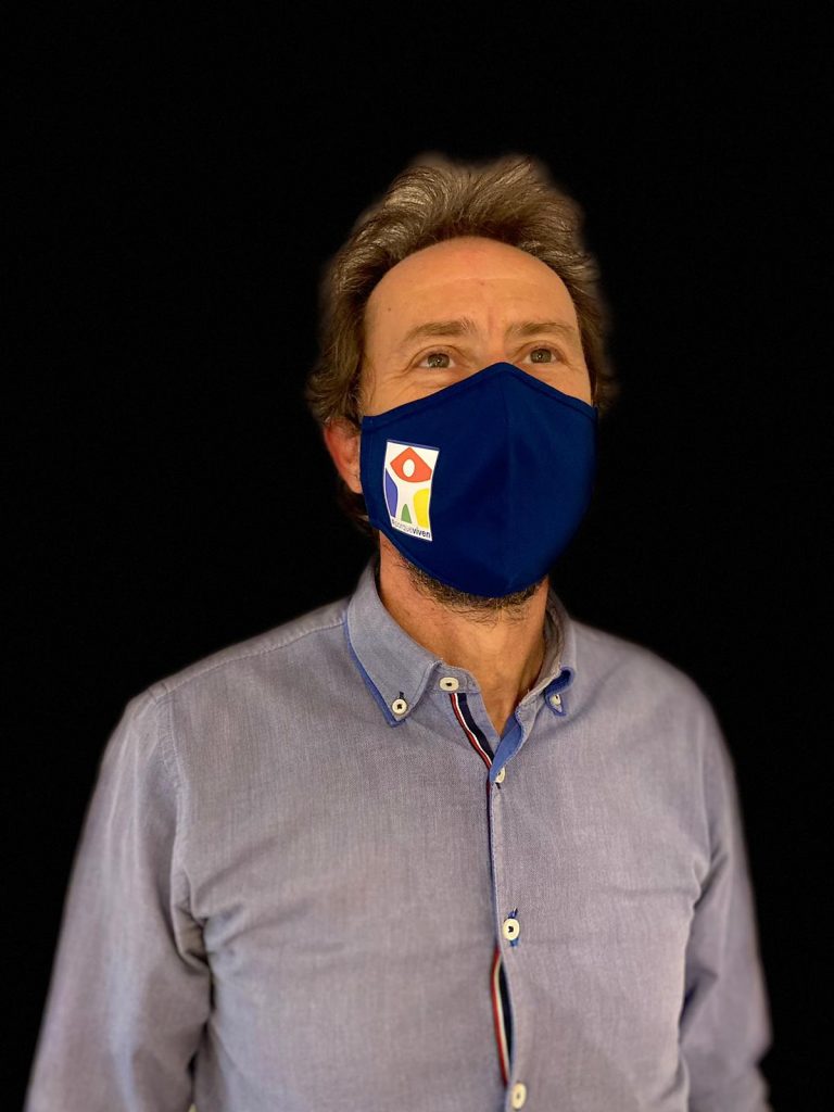 Un hombre con mascarilla azul de la Fundación porqueViven, luce camisa celeste, posando sobre fondo negro en Madrid