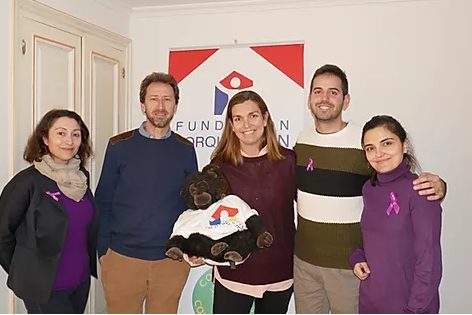 Cinco personas posan junto a un cartel de la Fundación Prodanvi; visten lazos y ropa morada en apoyo