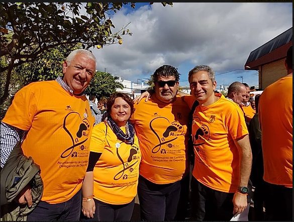 Cuatro adultos con camisetas naranjas de la sonríen al aire libre, mostrando unidad