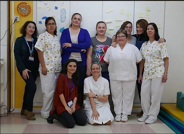 Equipo Fundación porqueViven, diez mujeres, algunas en uniforme blanco, posan juntas en su espacio de cuidados pediátricos