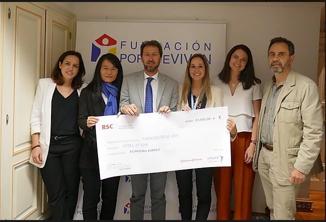 Seis personas sonríen mientras entregan un cheque simbólico ante el logo