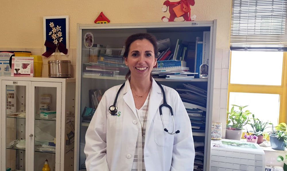 Una doctora de la sonríe en una sala luminosa con libros, material médico y plantas, en Madrid