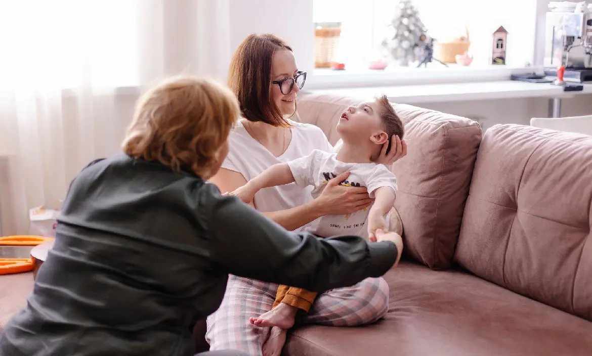 Una madre sostiene a su hijo en un sofá, acompañado por el equipo Fundación porqueViven, recibiendo cuidados paliativos pediátricos en casa