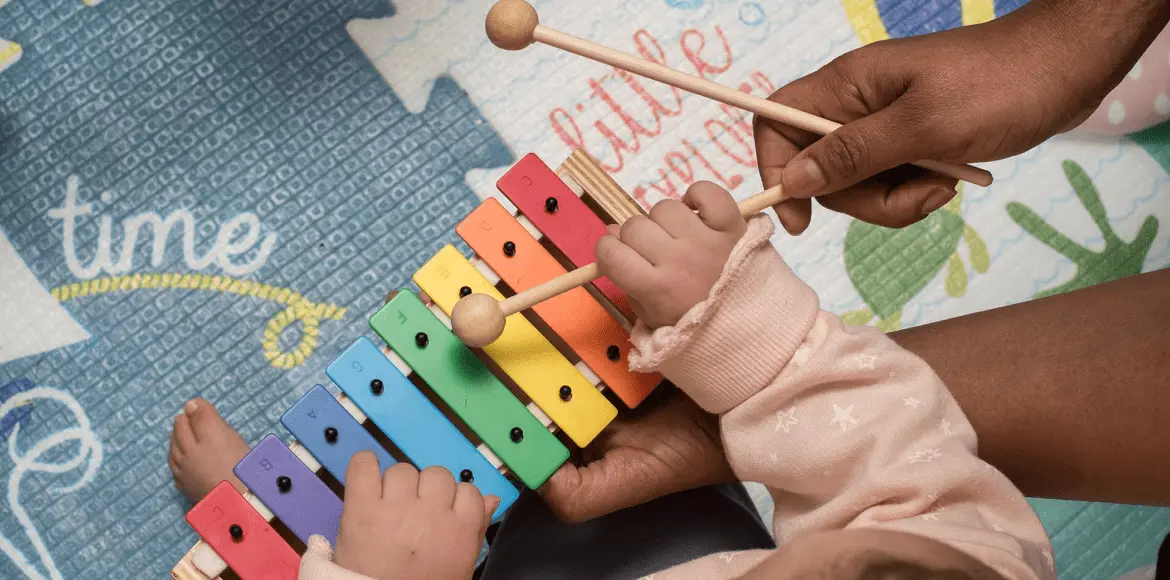 Manos de un adulto y un niño tocan juntos un xilófono colorido, reflejando el apoyo
