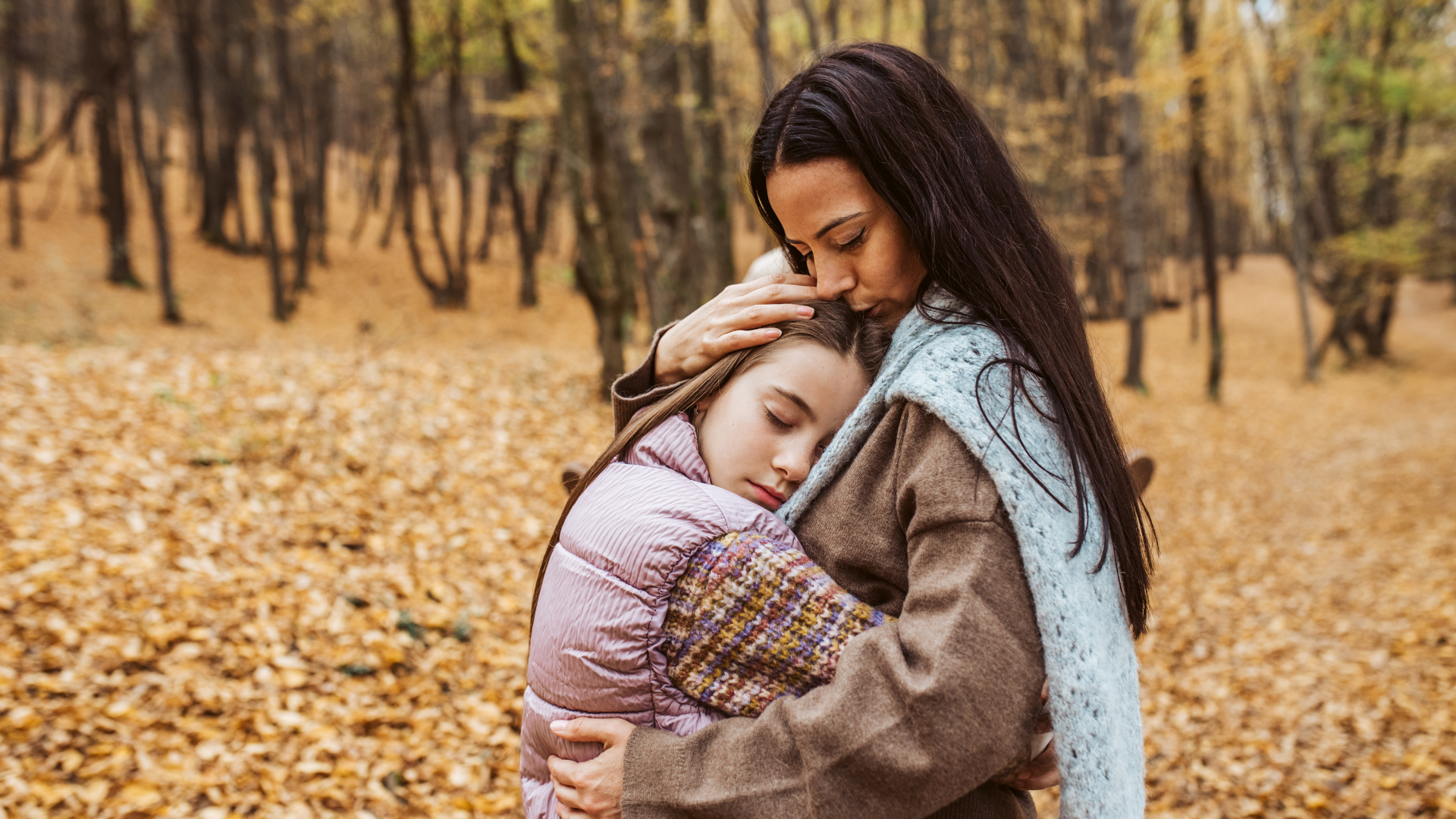 Una mujer de la Fundación porqueViven abraza y besa con ternura a una niña, caminando juntas entre hojas caídas en otoño