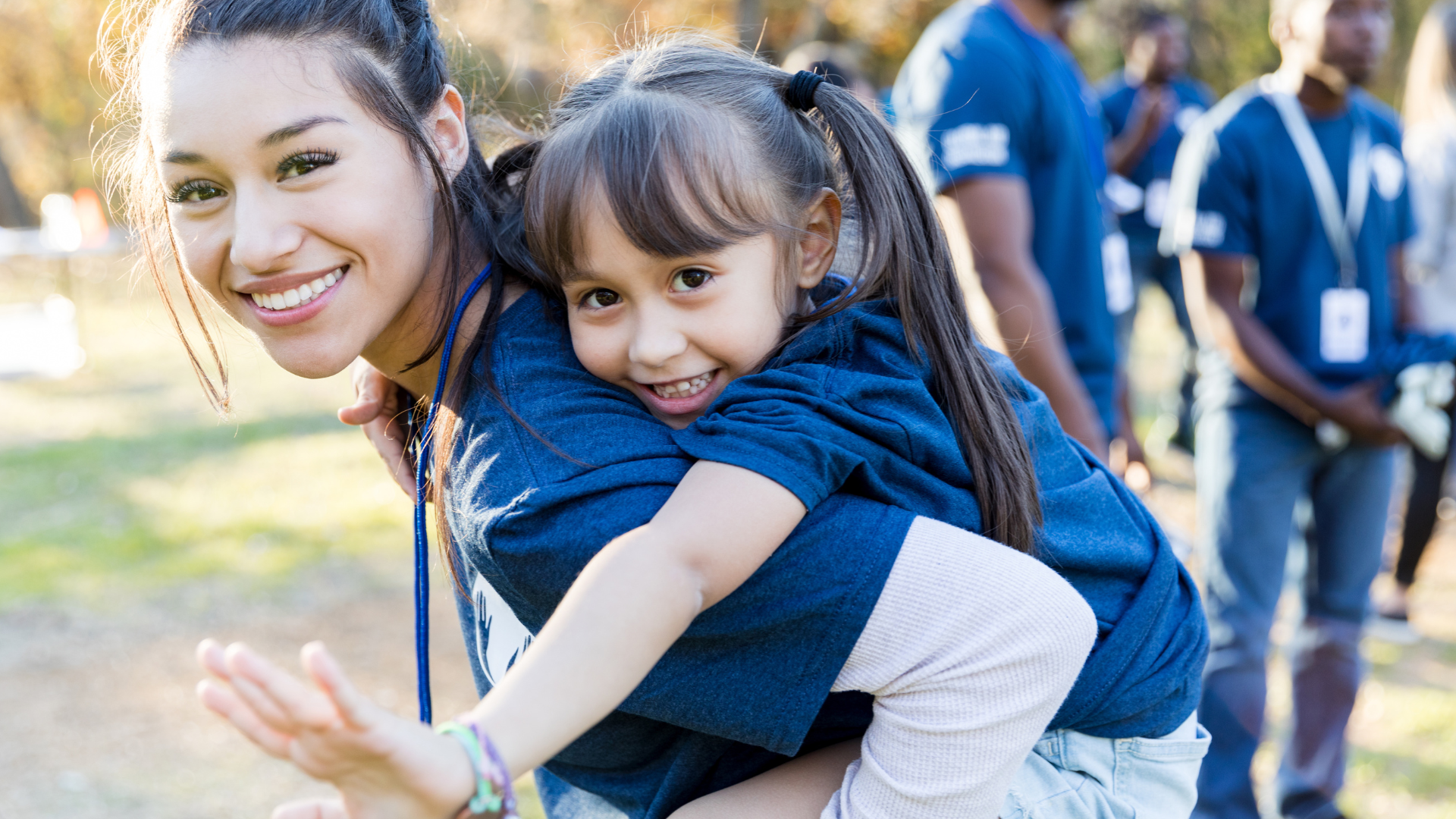 Un voluntario Fundación porqueViven lleva a una niña sonriente durante una jornada lúdica de cuidados paliativos en Madrid